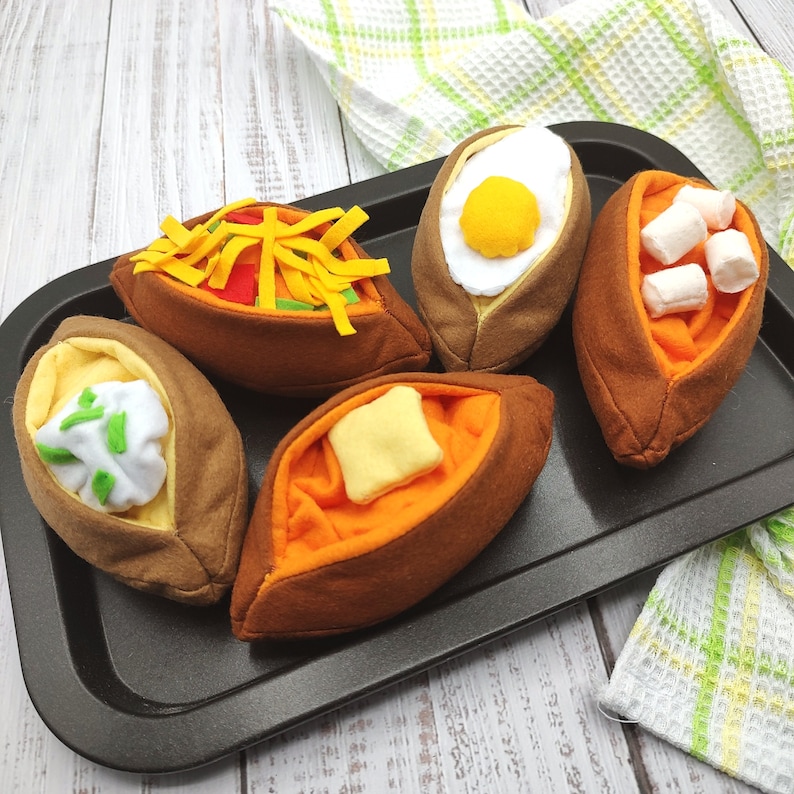 Puede incluir: Cinco alimentos de fieltro en una bandeja negra. Los alimentos tienen forma de patatas y est&aacute;n rellenos de diferentes ingredientes, como queso, crema agria y un huevo frito.