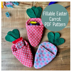 Może przedstawiać: Trzy filcowe pojemniki na słodkości w kształcie wielkanocnych marchewek. Jeden jest różowy w białe kropki, drugi jest różowy w biało-różową kratkę, a ostatni jest różowy w białe kropki z zielonym filcowym wierzchołkiem. Tekst "Fillable Easter Carrot PDF Pattern" znajduje się na turkusowym tle.