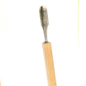 May include: A woodworking chisel with a metal blade and a wooden handle. The blade is a dull silver color, and the handle is a light brown. The chisel is designed for shaping and cutting wood.