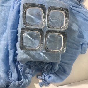 May include: A set of four clear glass square candle holders. The candle holders are arranged in a 2x2 grid.