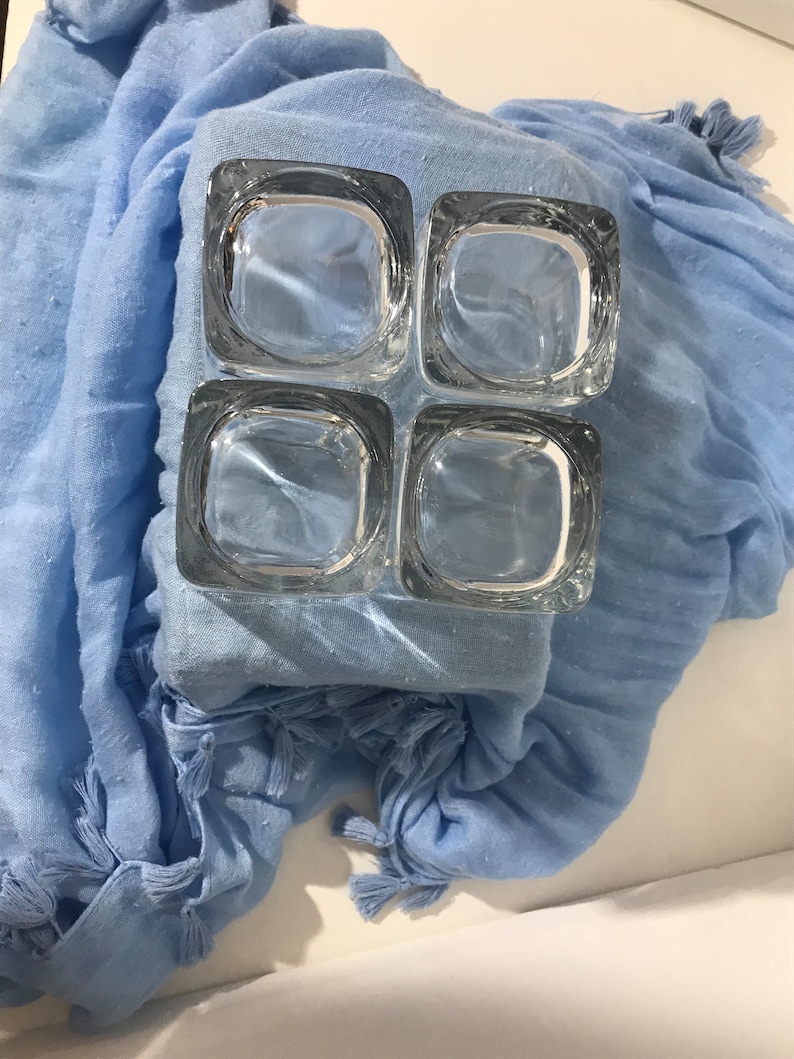 May include: A set of four clear glass square candle holders. The candle holders are arranged in a 2x2 grid.