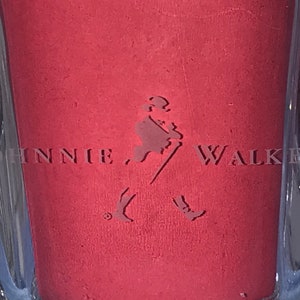May include: A close-up of a red bottle with the Johnnie Walker logo embossed on the front. The logo features a man walking with a stick and two birds flying behind him.