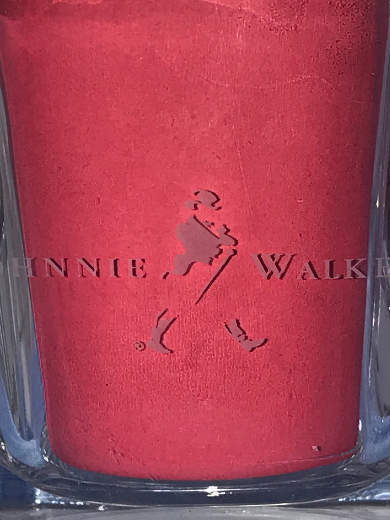 May include: A close-up of a red bottle with the Johnnie Walker logo embossed on the front. The logo features a man walking with a stick and two birds flying behind him.