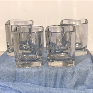 May include: Four clear glass tumblers with a square shape. The tumblers are etched with the words "Johnnie Walker Red Label".