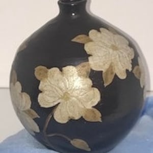 May include: A black ceramic vase with a rounded body and a narrow neck. The vase is decorated with white and gold floral designs.