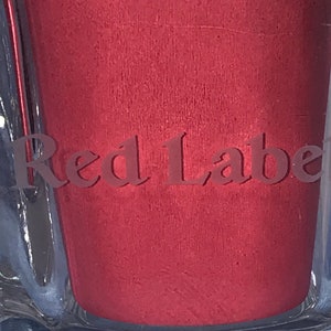 May include: Close-up of a red glass bottle with the words "Red Label" embossed on the front.