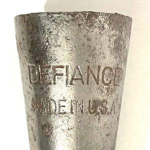 May include: Close-up of a metal tool with the word "DEFIANCE" and "MADE IN USA" stamped on its surface. The tool has a tapered shape and a worn, textured appearance.