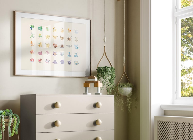 May include: A framed print of a colorful illustration of Pokemon characters. The print is hanging on a light beige wall above a white dresser with four drawers. There are two hanging plants in the corner of the room.