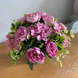 May include: An artificial flower arrangement featuring pink peonies and hydrangeas, with green foliage.