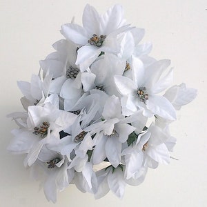 May include: A cluster of white artificial flowers with a star-shaped design. The flowers are arranged in a circular shape and have a delicate, silky texture.