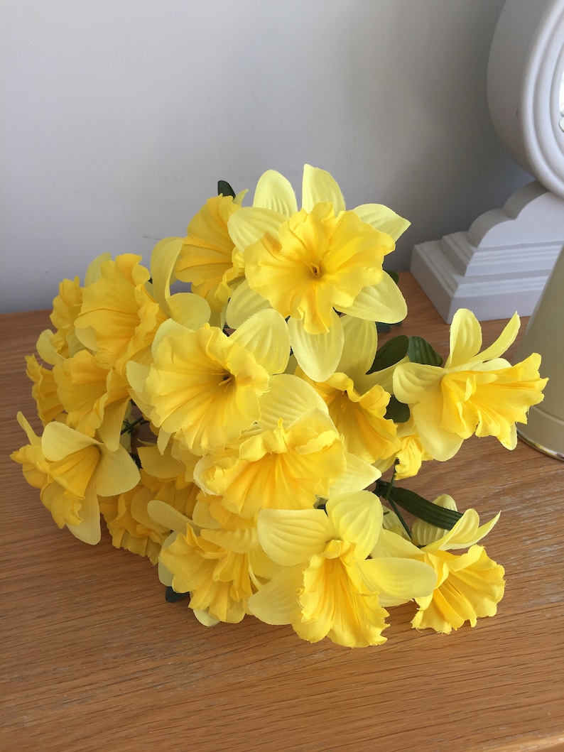 May include: A bouquet of yellow daffodils with green stems. The flowers are arranged in a cluster and have a soft, delicate appearance.