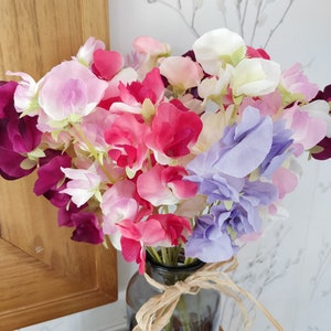Puede incluir: Un ramo de flores de guisante dulce en un jarr&oacute;n de vidrio. Las flores son en tonos de rosa, morado y blanco.