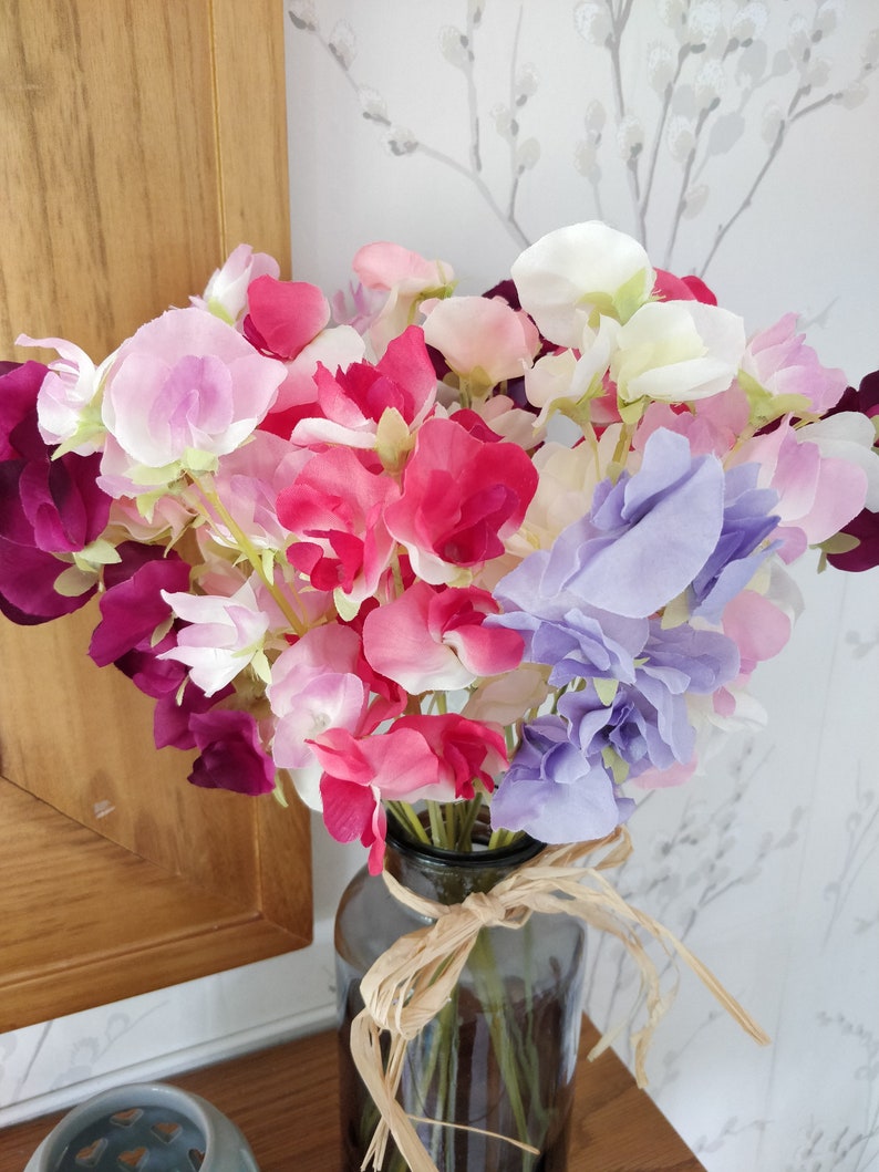 Puede incluir: Un ramo de flores de guisante dulce en un jarr&oacute;n de vidrio. Las flores son en tonos de rosa, morado y blanco.