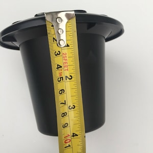 May include: Black plastic pot with a 10 cm diameter, measured with a yellow tape measure.