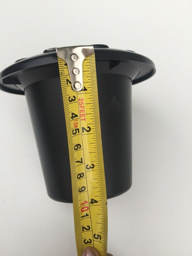 May include: A black plastic container, approximately 4.75 inches tall, is measured with a yellow tape measure. The container has a wide, flat top and a tapered cylindrical body. The tape measure shows the height of the container.