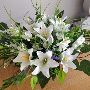 May include: A bouquet of white lilies with green leaves and purple flowers.