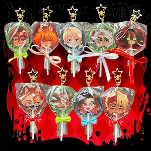 May include: A collection of nine circular acrylic charms shaped like lollipops, each featuring a unique anime-style character face. Every charm is individually wrapped in clear plastic, tied with a small ribbon, and topped with a gold star clasp.