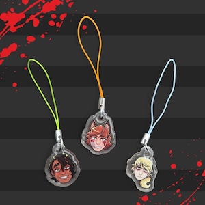 May include: Three clear acrylic charms with cartoon character faces, each with a different expression. The charms are attached to colorful lanyards in green, orange, and blue. The background is black with red splatter and gray stripes.