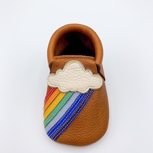 May include: Brown leather baby moccasins with a rainbow and cloud applique.