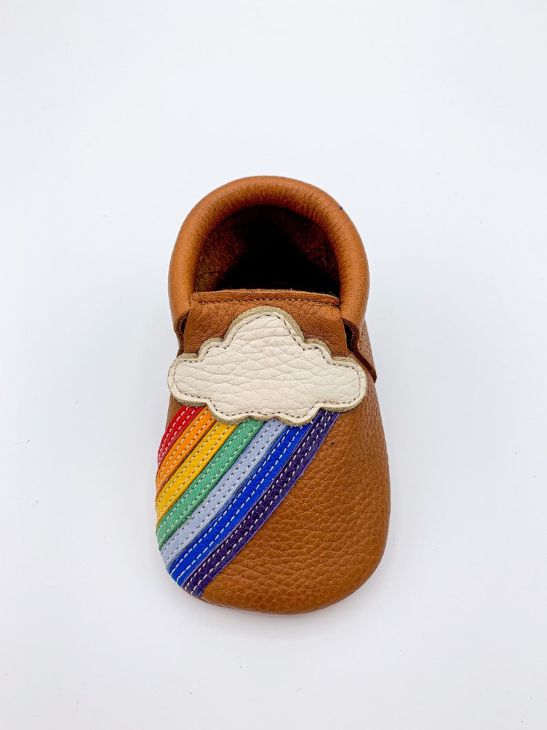 May include: Brown leather baby moccasins with a rainbow and cloud applique.
