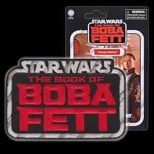 Pode incluir: Um remendo bordado preto e cinza com o texto "STAR WARS THE BOOK OF BOBA FETT" em letras vermelhas. O remendo tem um padrão de camuflagem.