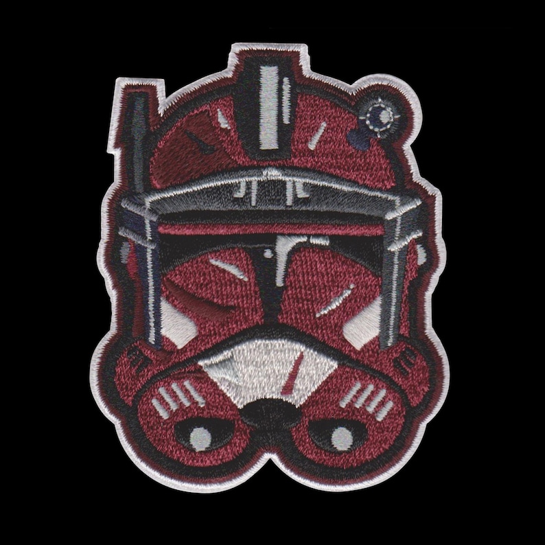 Puede incluir: Parche bordado con un dise&ntilde;o de casco granate y negro. El parche tiene un borde blanco y costuras detalladas. El casco tiene una visera y otros detalles. El parche est&aacute; sobre un fondo negro.