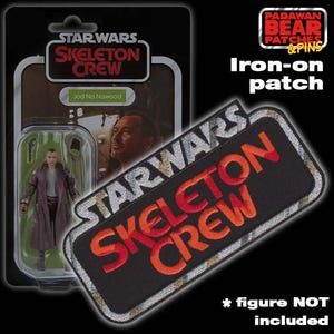 May include: Iron-on patch featuring the Star Wars Skeleton Crew logo in red and orange lettering on a black background with silver accents. The text "STAR WARS" is above the logo and "CREW" is below the logo. The patch is on a white background with a Star Wars action figure in the background.