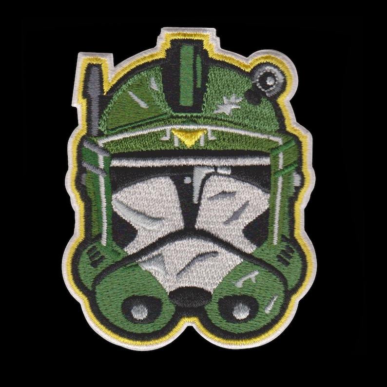 Puede incluir: Parche bordado con un dise&ntilde;o de casco verde y blanco con detalles amarillos y negros. El parche tiene un estilo detallado de dibujos animados, sobre un fondo negro. La forma distintiva del casco sugiere un tema de ciencia ficci&oacute;n o fantas&iacute;a.