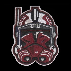 Puede incluir: Parche bordado con un dise&ntilde;o de casco granate y negro con detalles blancos y grises. El parche tiene una apariencia detallada y texturizada, con un borde negro. El dise&ntilde;o recuerda a un tema militar o de ciencia ficci&oacute;n.