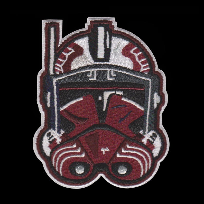 Puede incluir: Parche bordado con un dise&ntilde;o de casco granate y negro con detalles blancos y grises. El parche tiene una apariencia detallada y texturizada, con un borde negro. El dise&ntilde;o recuerda a un tema militar o de ciencia ficci&oacute;n.