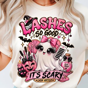 Op de afbeelding: Een crèmekleurig t-shirt met een afbeelding van een witte geest met een roze strik, lange wimpers en wimpertools. De tekst luidt LASHES SO GOOD IT'S SCARY LASH ARTIST, omringd door roze pompoenen, vleermuizen en een flesje met toverdrank.