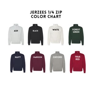 May include: Color chart of Jerzees 1/4 zip sweatshirts in various colors, including ash, black, white, forest green, navy, maroon, oxford, and true red. Each sweatshirt has a quarter-zip collar and the color name printed on the front.