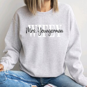 May include: Grey sweatshirt with the text "WIFEY" in large white letters and "Mrs. Youngerman" in black cursive writing below.
