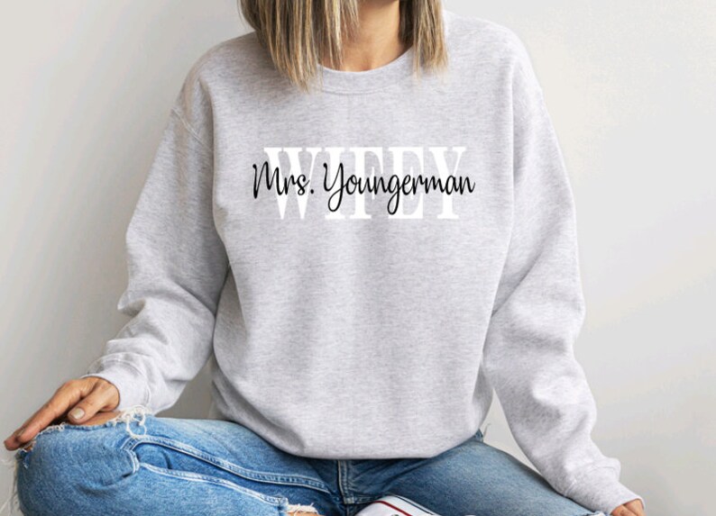 May include: Grey sweatshirt with the text "WIFEY" in large white letters and "Mrs. Youngerman" in black cursive writing below.