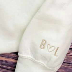 May include: White sweatshirt with a cream coloured embroidered design on the sleeve that says "B&hearts;L"