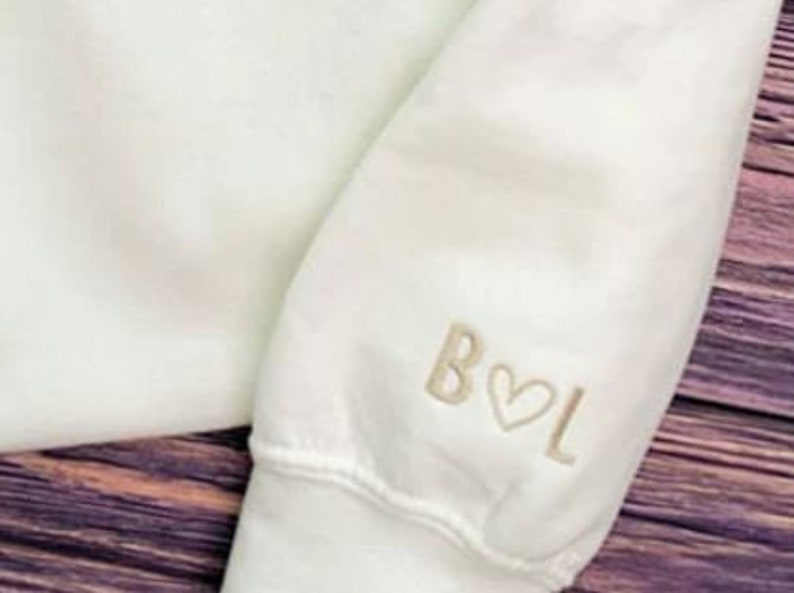 May include: White sweatshirt with a cream coloured embroidered design on the sleeve that says "B&hearts;L"
