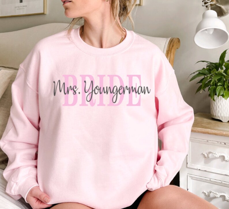 May include: Pink sweatshirt with the text "Mrs. Youngerman" and the word "BRIDE" in pink letters.