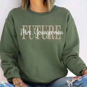 May include: A green sweatshirt with the text "FUTURE Mrs. Youngerman" in brown and white lettering.