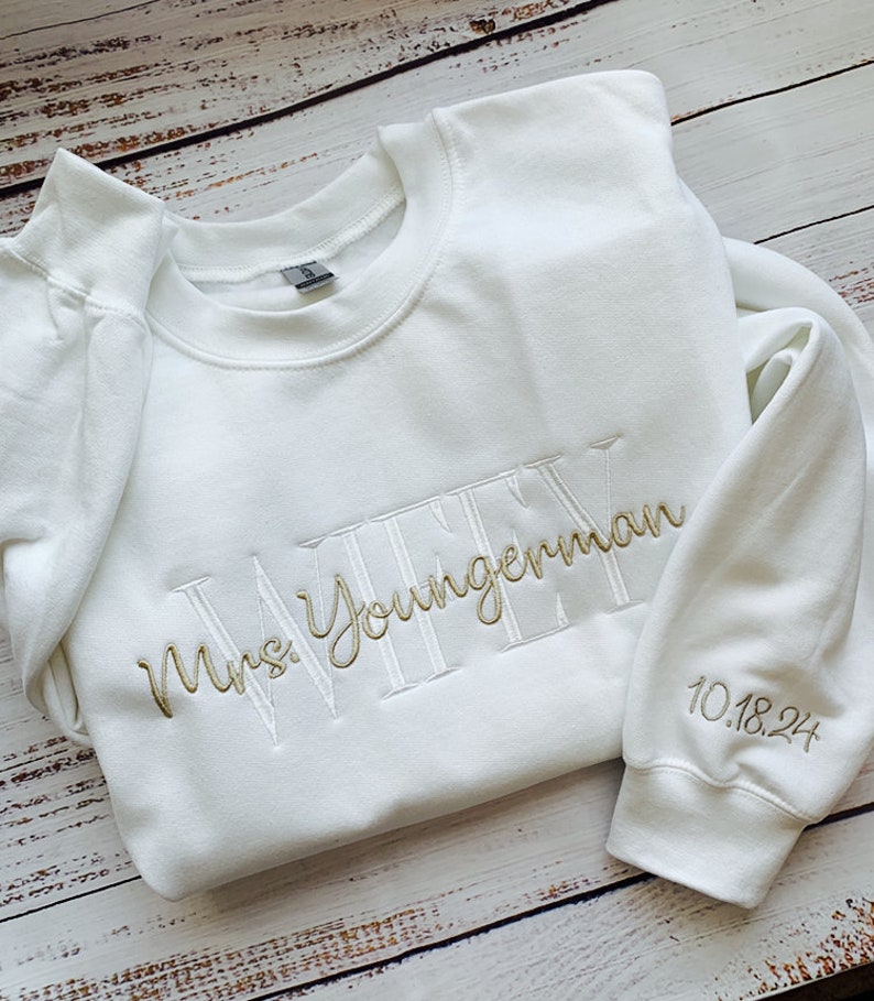 May include: White sweatshirt with gold embroidery that says "Mrs. Youngerman" and "10.18.24" on the sleeve.