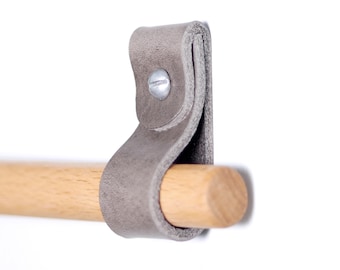 Könnte beinhalten: Nahaufnahme eines grauen Lederriemens mit einer silbernen Schraube, der einen natürlichen Holzdübel hält. Der Lederriemen ist an der Wand befestigt und schafft ein minimalistisches Design. Der Holzdübel hat einen Durchmesser von ca. 2,5 cm.