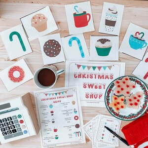 以下が含まれることがあります： クリスマスをテーマにしたスイーツショップのメニュー。レジ、様々なスイーツ、価格表が載っています。メニューは、キャンディーケーン、ホットチョコレート、チョコレートカップケーキ、ジンジャーブレッドクッキーなどがあります。レジは白で、黒いボタンとディスプレイが付いています。