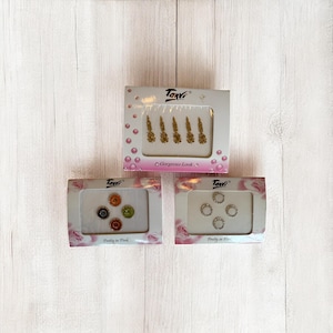 Op de afbeelding: Drie dozen met decoratieve gezichtsjuwelen. De bovenste doos bevat goudkleurige bloemmotieven, de middelste doos heeft kleurrijke ronde juwelen en de onderste doos zilverkleurige ronde juwelen. De dozen zijn voorzien van het merk "Tanvi".