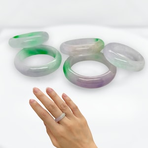 May include: Four jade bangles in shades of green and purple. The bangles are stacked on top of each other.