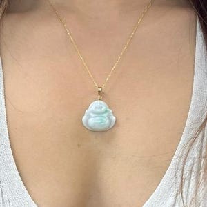 May include: A gold chain necklace with a light green jade pendant in the shape of a sitting Buddha. The necklace is 18 inches long.