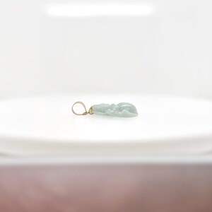 May include: A light green jade pendant carved with a detailed design, set in a gold tone metal bail.