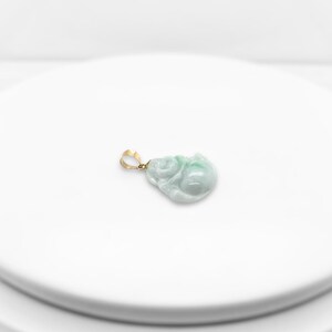 May include: A jade pendant in the shape of a sitting Buddha, carved from green jade with a gold bail.