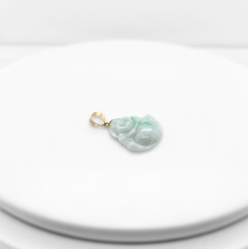 May include: A jade pendant in the shape of a sitting Buddha, carved from green jade with a gold bail.