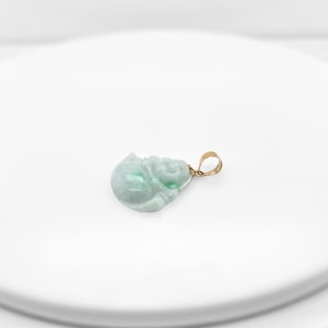 May include: A green jade pendant carved in the shape of a sitting Buddha. The pendant is attached to a gold chain.