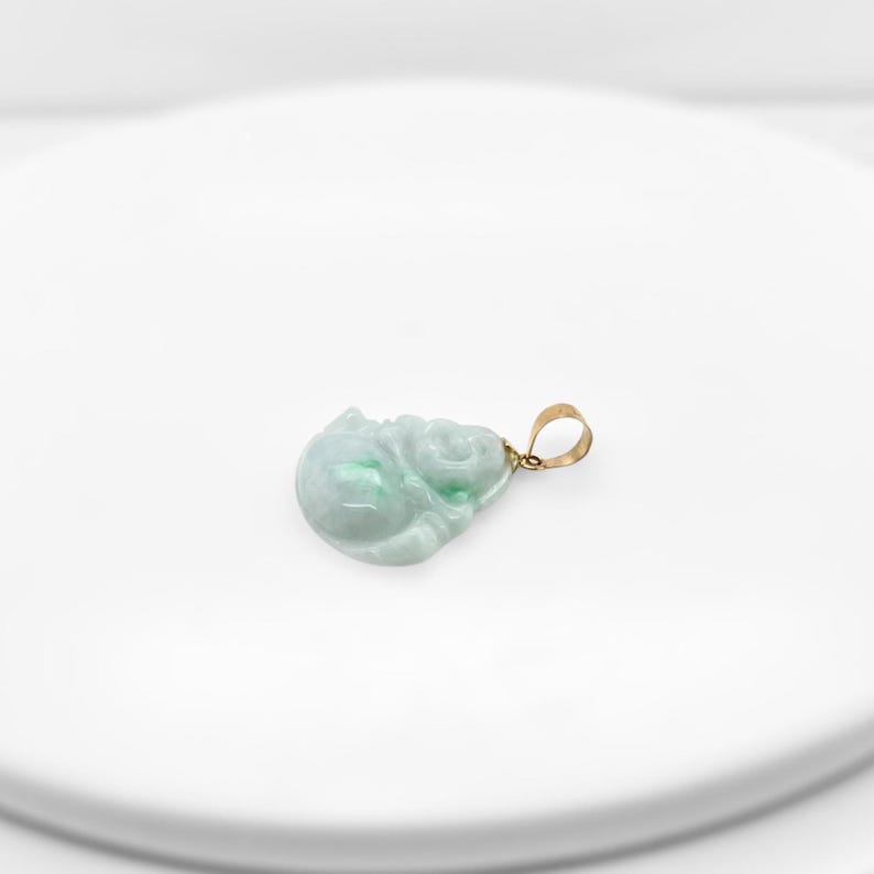 May include: A green jade pendant carved in the shape of a sitting Buddha. The pendant is attached to a gold chain.