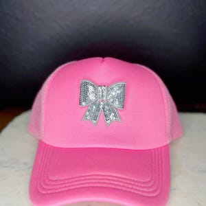 Peut inclure: Casquette de camionneur rose vif ornée d'un nœud en sequins argentés. La casquette présente une visière incurvée et un dos en filet. Un accessoire de mode pour un look décontracté, alliant style et confort.